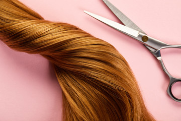 Top view of twisted brown hair with scissors on pink background