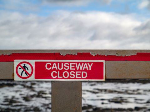 Warning causeway closed sing on a wooden barrier, Cloudy sky in the background.