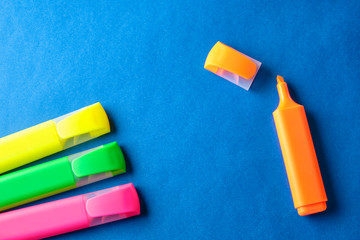 Multi colored highlighters at blue background with copy space
