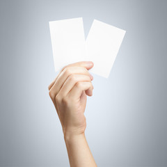 Hand holding pair of paper or plastic cards (tickets, flyers, invitations, coupons, etc.) on gray background