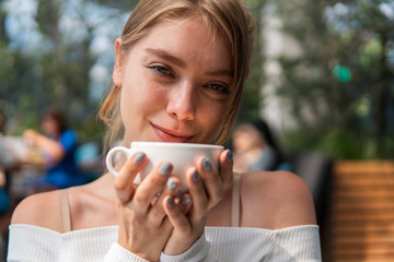 Pretty young blond woman with coffe cup in cafe smile and laugh.