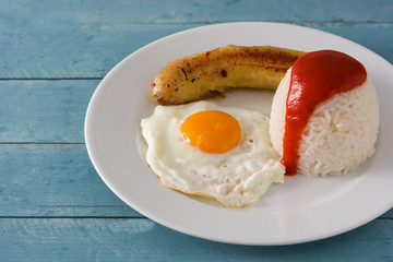 Arroz a la cubana Typical Cuban rice with fried banana and fried egg on a plate on wooden table. 