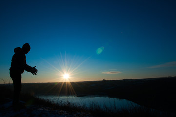  Silhouetted men on a background of blue sky and sunny sunset. Man with hands up