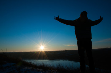 Fototapeta premium Silhouetted men on a background of blue sky and sunny sunset. Man with hands up