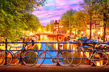 Alte Fahrräder auf der Brücke in Amsterdam, Niederlande, gegen einen Kanal während des Sonnenuntergangs in der Sommerdämmerung. Amsterdam-Postkartenikonenansicht.