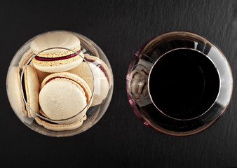 Macaroons in a glass. A glass of young red wine. Top view, black stone background.