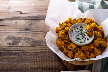 baked cauliflower with sour cream sauce and greens on brown wooden background