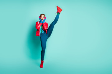 Full body photo of crazy yelling lady raise leg up high shocking flexibility after first gym training wear red overcoat gloves pink ear muffs pants shoes isolated teal color background