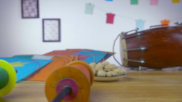 Beautiful designer reel Charkhis rolling on a wooden table - Makar Sankranti festival. Closeup shot of rolling charkhis with colorful paper kites  til ladoos  and dholak in the background on Indian...