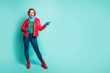 Full body photo of beautiful lady directing fingers empty space offer sale prices final season wear red overcoat blue scarf pink ear covers pants boots isolated teal color background