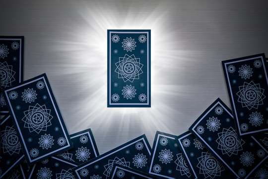 Blue Tarot Cards Scattered On White Wood, With A Card In The Center That Gives Off Light