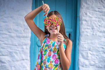Smiling brunette young girl holding and closing her eyes with spiral colorful candy.