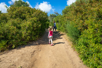 four years age blonde child with pink shirt walking, next to her mother woman turned and looking on a path in the forest of Cadiz, Spain