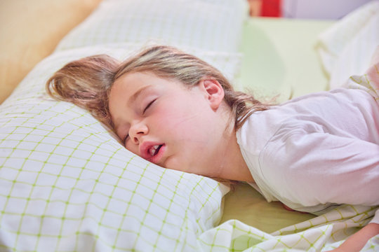 funny expression face with open mouth of blonde caucasian five years old girl,  sleeping on king bed