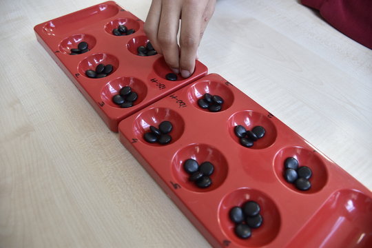 A table game of a beige color on a table: "mangala". and hands of people playing mangala