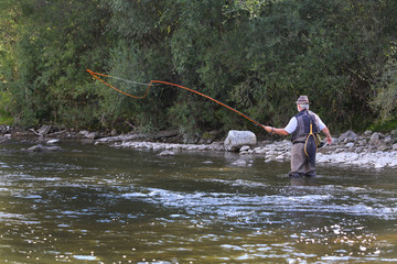 Fly fisherman using flyfishing rod in beautiful river.