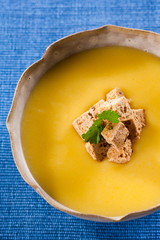 A bowl of vegetable soup with croutons on top, on a blue tablecloth