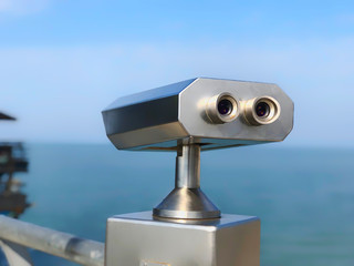 Paid outdoor tourist telescope made of stainless steel on the sea coast over blue sky background