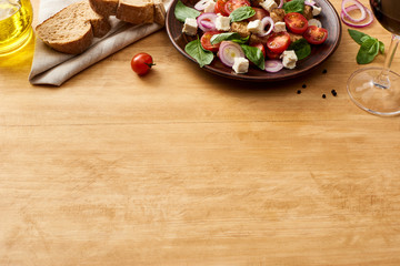 delicious Italian vegetable salad panzanella served on plate on wooden table near fresh ingredients, bread and red wine