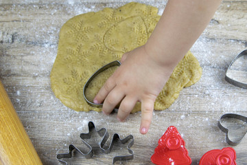 A child handstake out ginger cookies from rolled dough, cutter form a fir on a dark wooden...