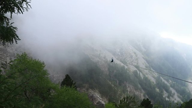 Young woman is going down the zip line among mountains and sea in clouds, Montenegro, 2019.