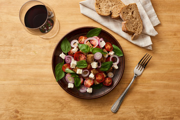 top view of delicious Italian vegetable salad panzanella served on plate on wooden table near fresh bread and red wine