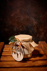 A jar full of sweet spices is covered with Kraft paper and tied with twine a medallion with the numbers of the new year 2020 is tied to it which stands on a wooden pallet