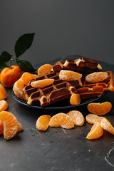 Soft Viennese waffles on a plate with tangerines on a dark gray background