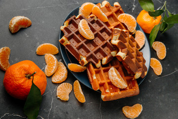 Soft Viennese waffles on a plate with tangerines on a dark gray background