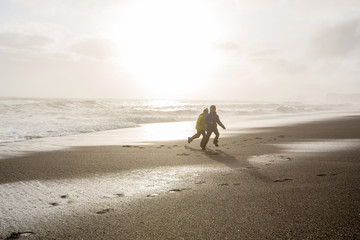 Children running from and to the ocean in black sand beach of Reynisfjara and the mount Reynisfjall in Iceland on a cold rainy day