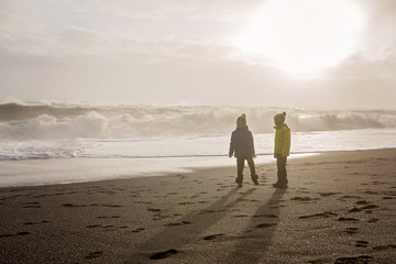 Children running from and to the ocean in black sand beach of Reynisfjara and the mount Reynisfjall...