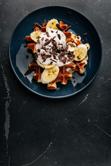 Viennese waffles on a plate, with a crumb of chocolate and slices of banana on a dark textured background.