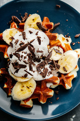 Viennese waffles on a plate, with a crumb of chocolate and slices of banana on a dark textured background.