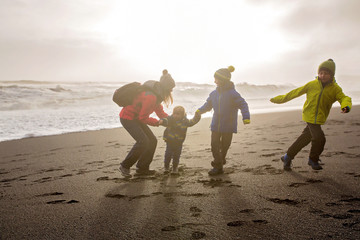 Family posing against the sun in black sand beach of Reynisfjara and the mount Reynisfjall in...