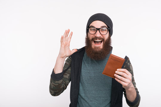 Photo of amazed young bearded man holding passport with tickets, time for travel