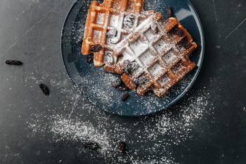 Viennese waffles, sprinkled with powdered sugar, on a dark textured table with a gray background
