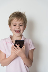 A cute child is laughing loudly, holding a cell phone in his hand.