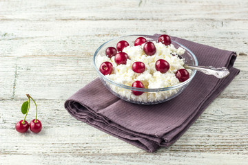 Breakfast from cottage cheese with cherry in transparent bowl on white wooden background