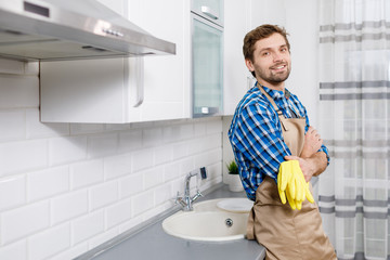 Contented young man posing leaning at the kitchen table top after intense household work