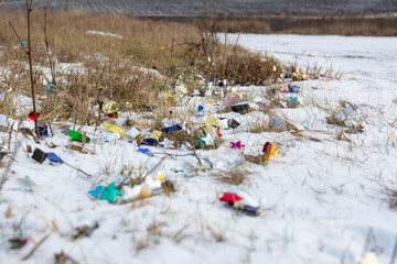 Confetti lie in the snow after the holiday. Natural meadow covered with garbage. Ecological problems.