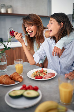 smiling gay lasbian couple at morning in kitchen eating breakfast