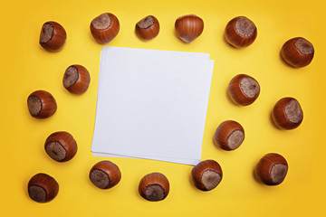 Unpeeled hazelnuts and sheet of paper on a yellow background. Flatley. Copy space.