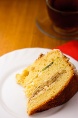 sponge cake on a white plate on a wooden background with a cup of black tea in a glass cup