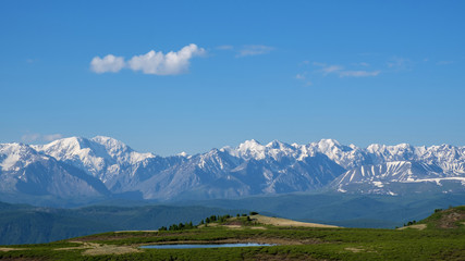 Small melt lake on a mountain plateau. Mountain oasis against the backdrop of a snowy ridge. Summer Altai.