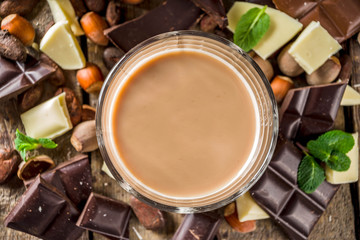 Sweet and strong alcohol drink. Chocolate liqueur with milk and dark chocolate pieces. Wooden background copy space