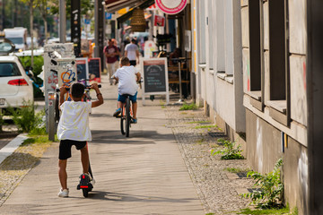 A little boy drives an e-scooter, in the background a boy with a bike, sunny day, summer weather, warm colors