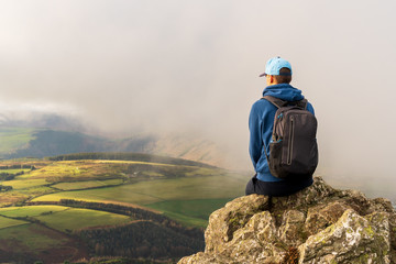 Male hiker resting at the edge of a cliff on a winter day in a misty landscape and enjoying the...