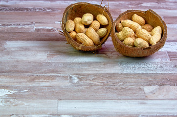 Peanuts lies in a coconut shell on a wooden table with place for text.Horizontal