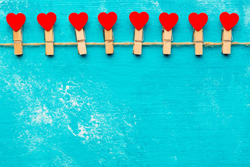 Valentine day background with red decorative hearts on rope and clothespins at rustic blue wooden table. Happy Valentine lovers day card mockup. Free space for your text