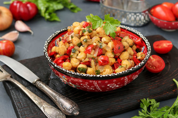 Garnish of chickpeas with pepper and tomatoes, a vegetarian dish rich in protein, located in a plate against a dark background horizontally